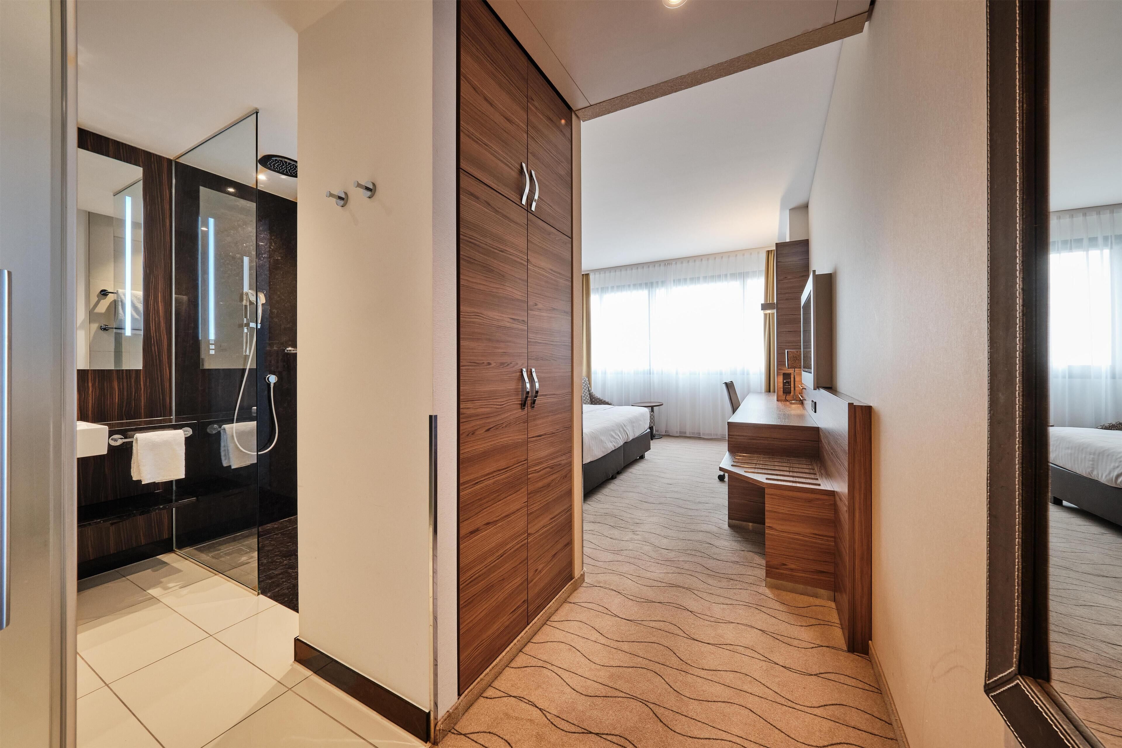Une chambre d’hôtel moderne équipée d’une salle de bain, d’un lit, d’un bureau et d’un grand miroir.