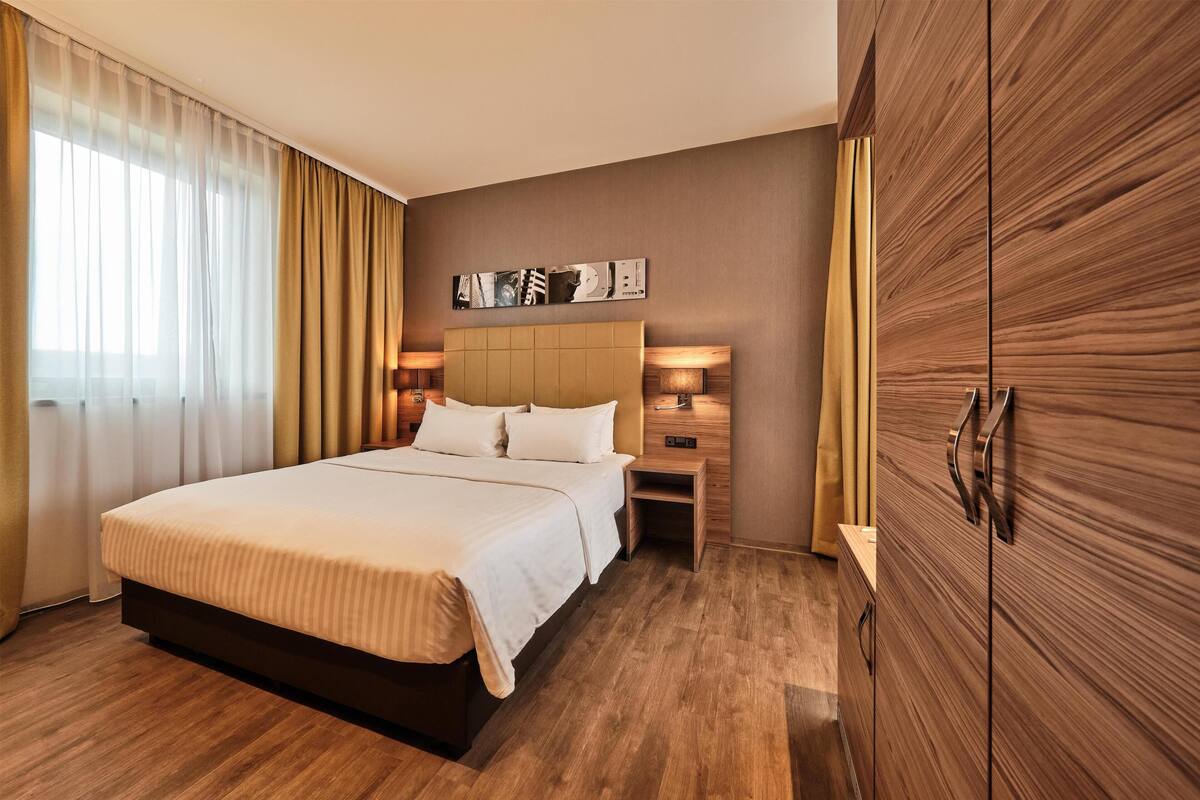 Habitación de hotel con una cama grande, armario de madera, lámparas de noche y una obra de arte colgada en la pared.