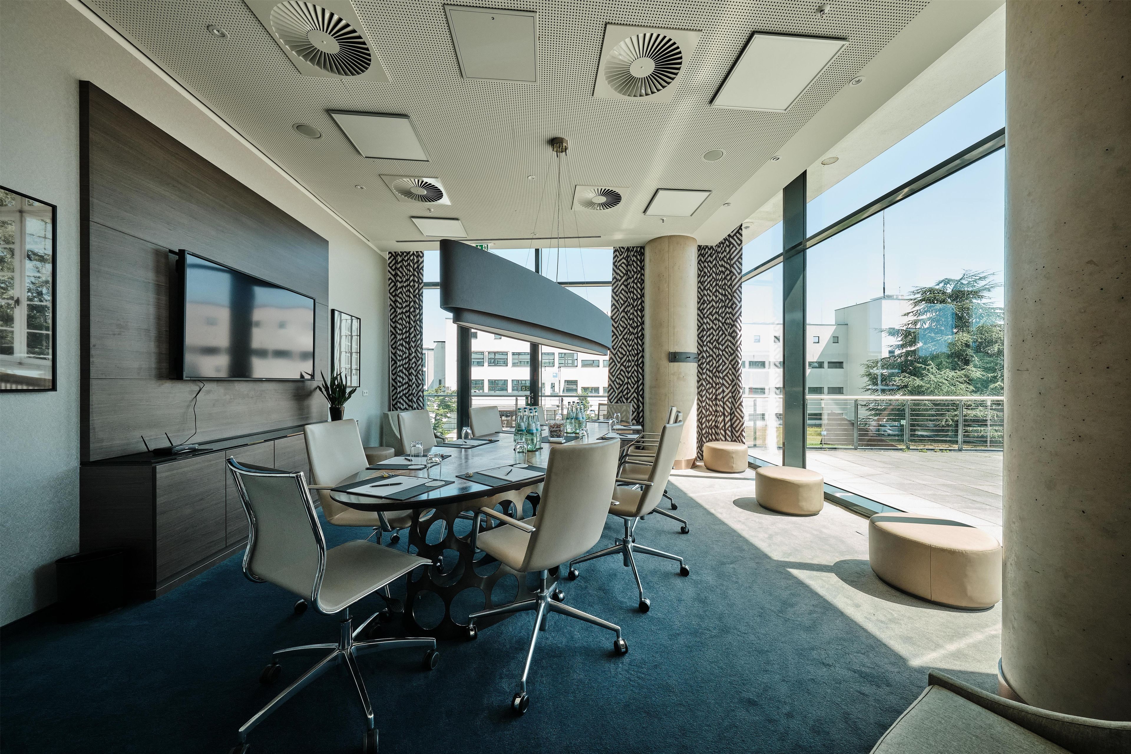 A modern conference room with a glass table, office chairs, and a ceiling with ventilation.