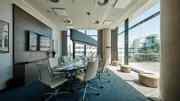 A modern conference room with a glass table, office chairs, and a ceiling with ventilation.