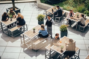 An outdoor patio with multiple wooden tables and benches, surrounded by potted plants. - Radisson Blu Hotel, Bonn (Bonn)