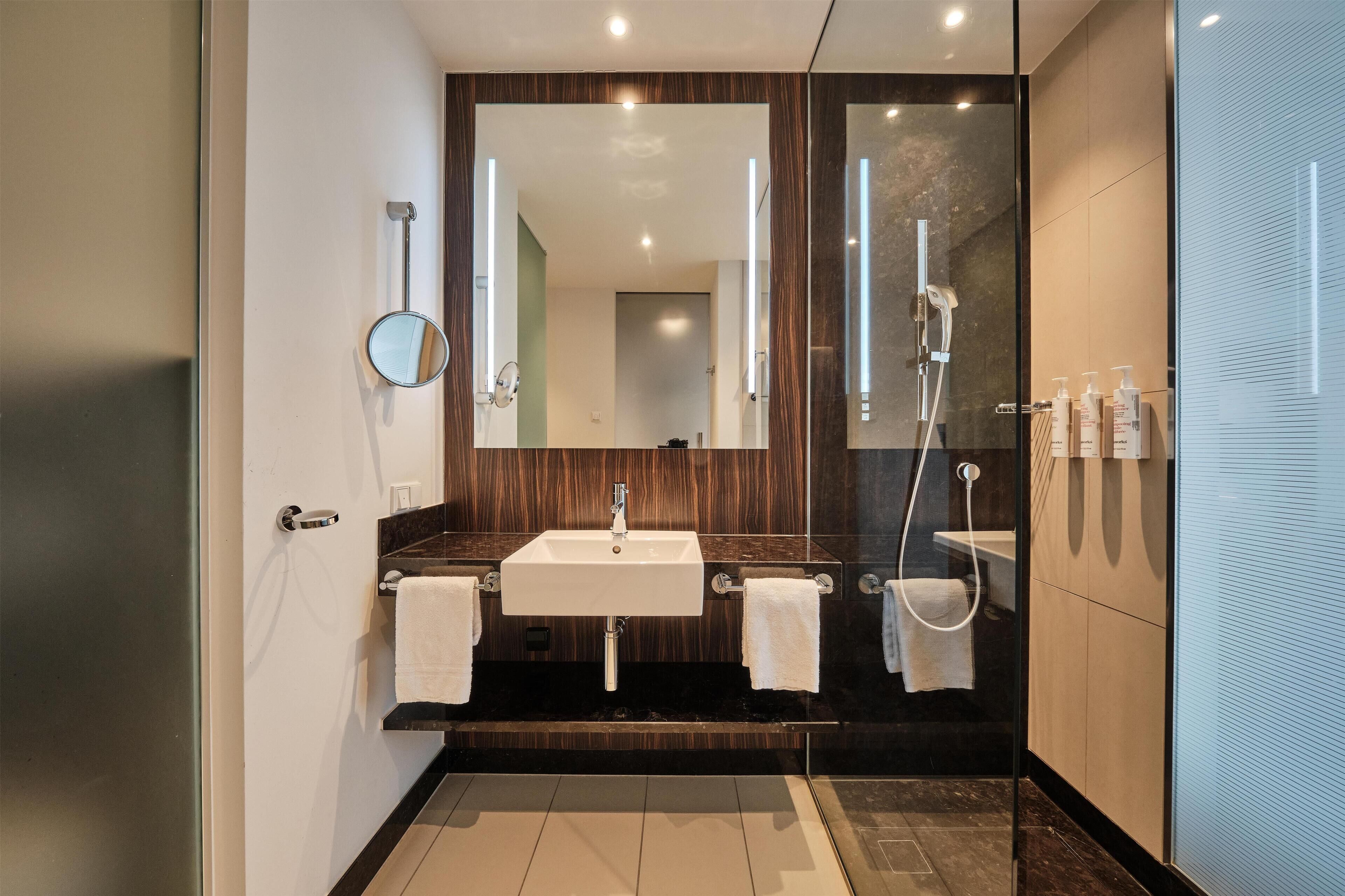 Un baño moderno con lavamanos doble, un espejo grande, cabina de ducha con mampara de vidrio y un perchero para toallas.