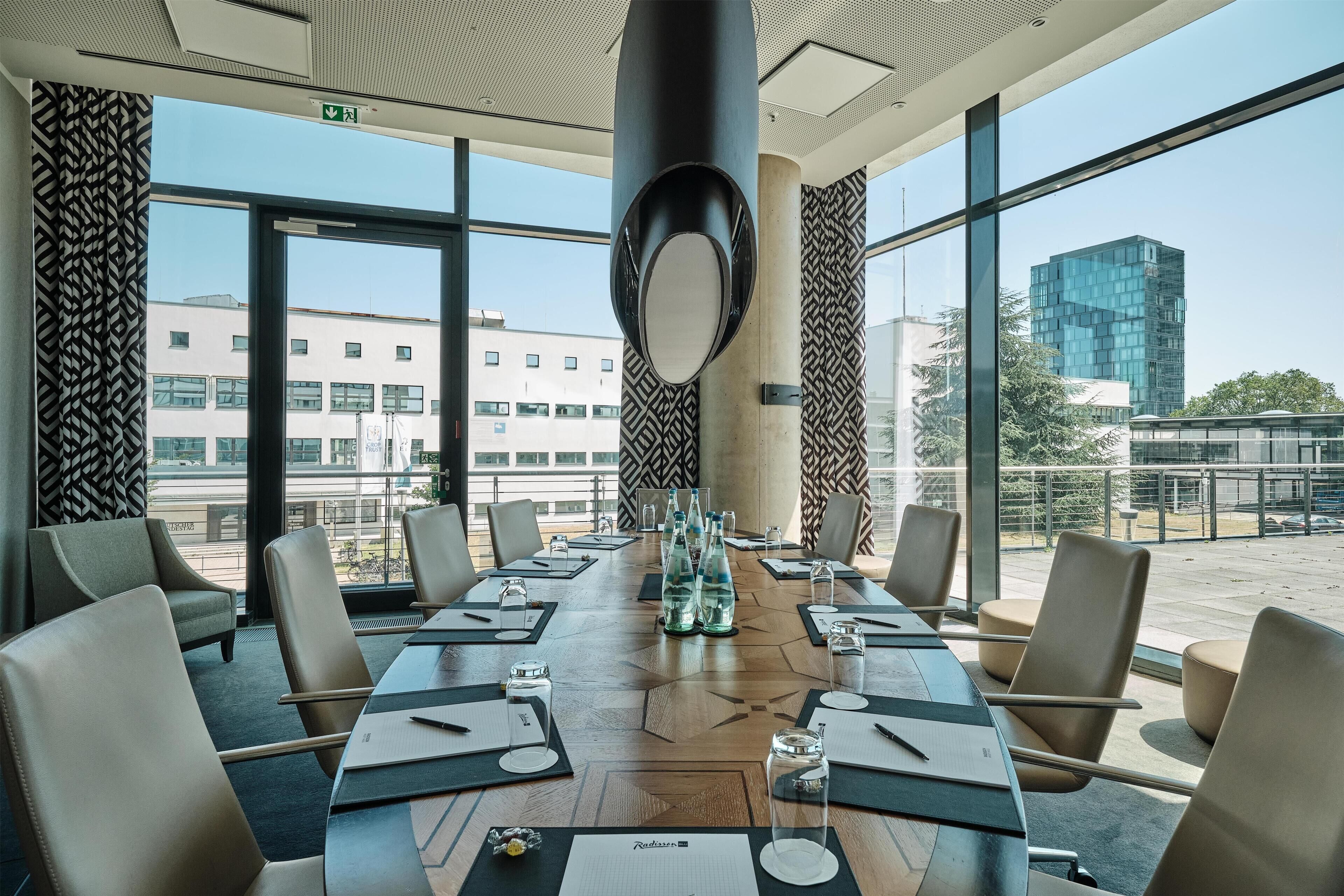 A conference room with a long table, chairs, and a large window with a view of buildings.