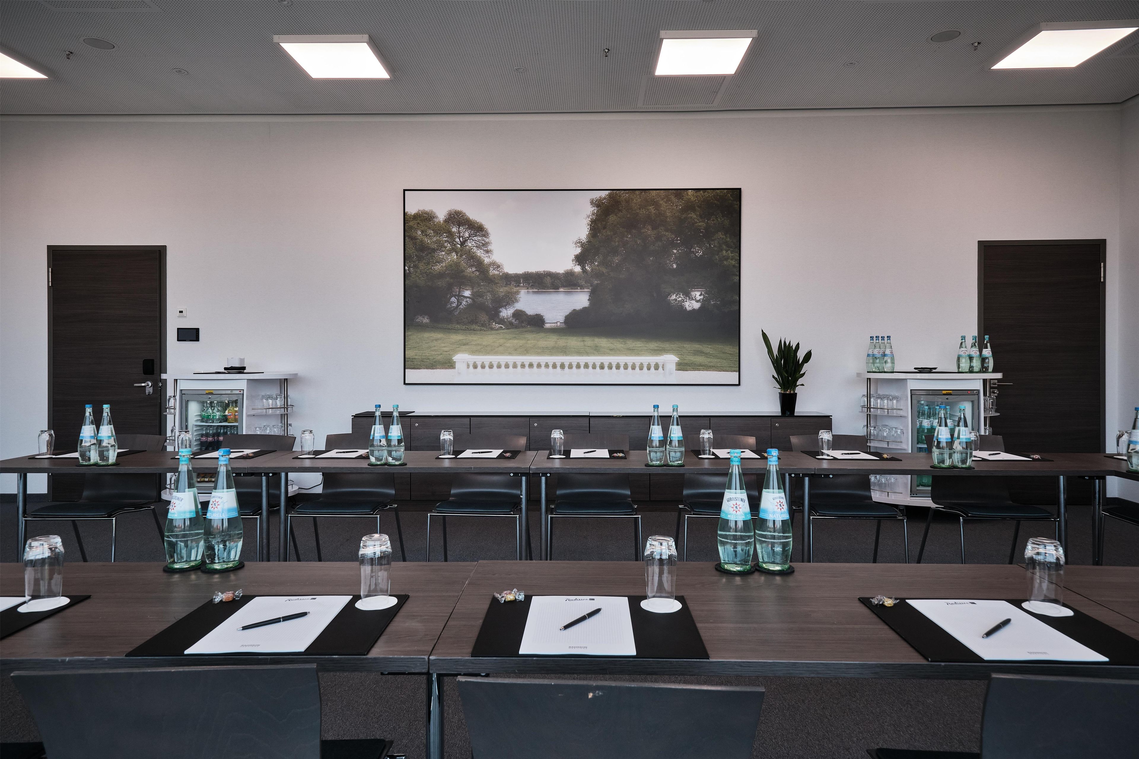 Un salón de conferencias con un amplio ventanal con vistas a un lago, equipado con botellas de agua y tarjetas de identificación sobre las mesas.