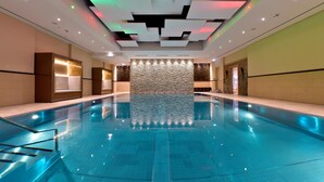 Una amplia piscina interior con un diseño moderno de techo, una pared de piedra al fondo y un ambiente bien iluminado.