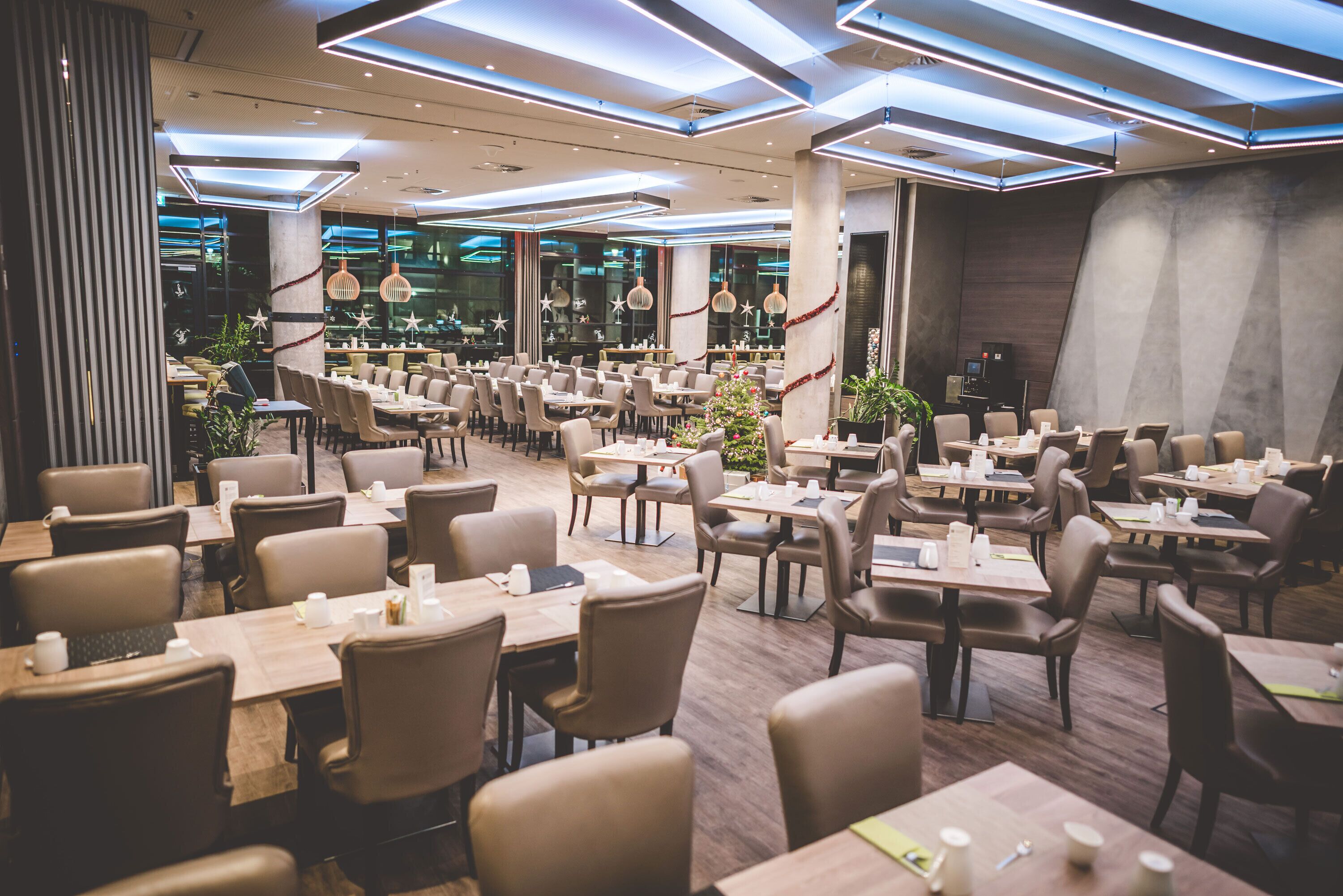 A modern restaurant with multiple dining tables and chairs, a Christmas tree, and contemporary lighting fixtures.
