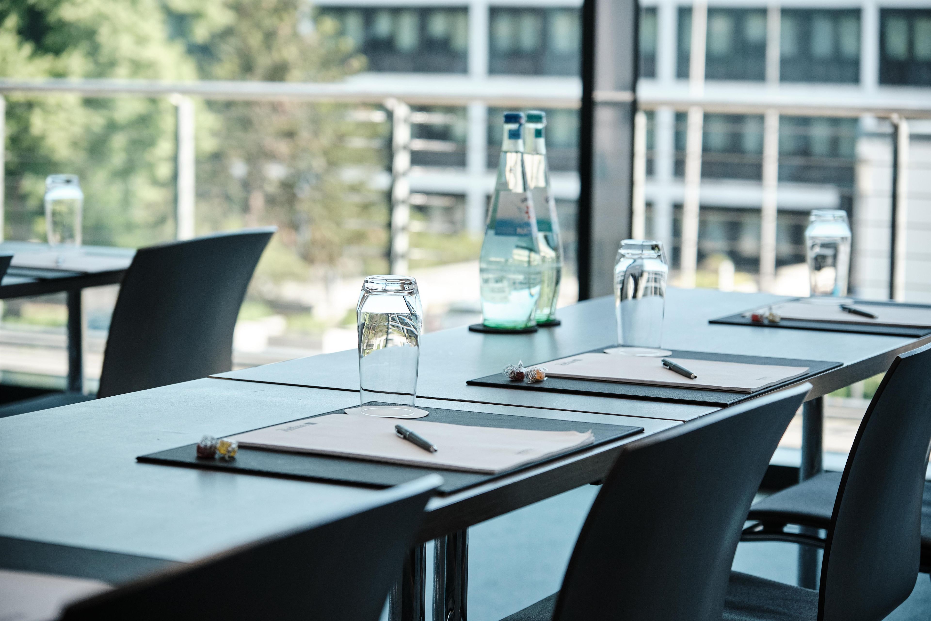 A conference table with water bottles, glasses, and notepads in a modern office setting with large windows.