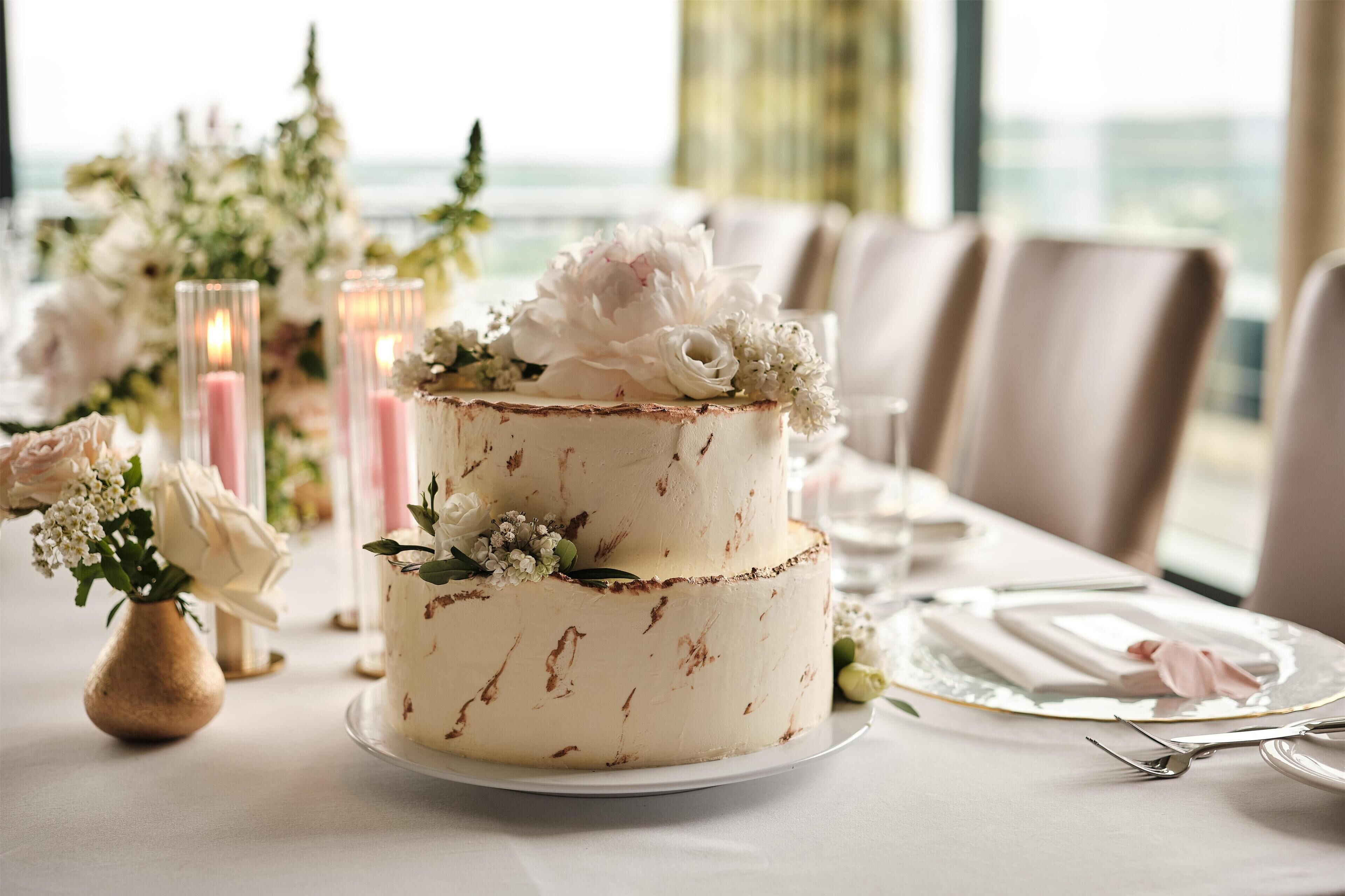 Un pastel de tres niveles decorado con flores sobre una mesa, rodeado de velas y flores.