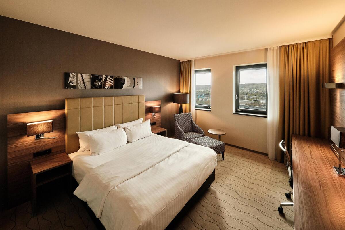 Habitación de hotel con una cama grande, un escritorio, una silla, una mesita y vistas a la ciudad.