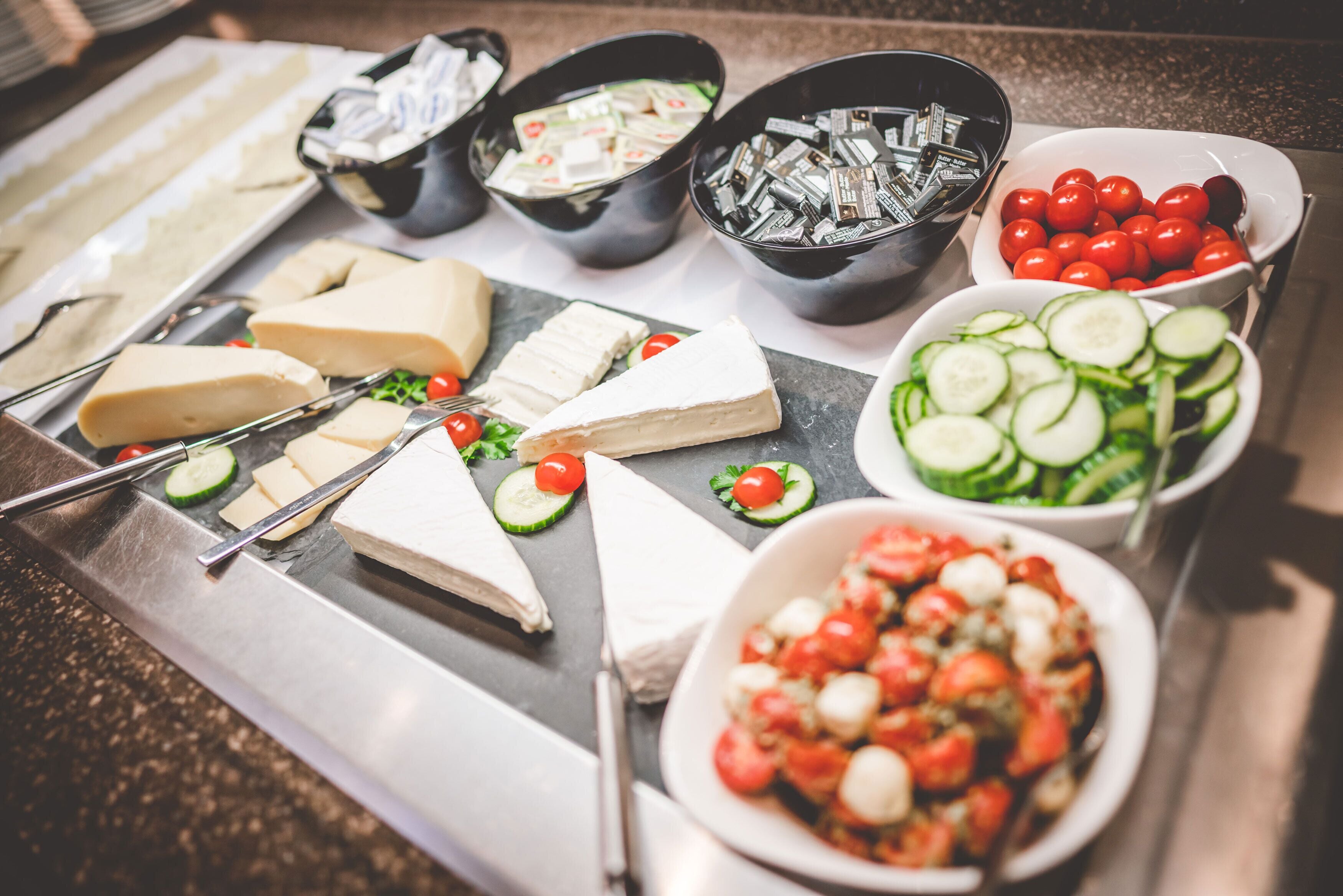 Een buffet met verschillende kazen, groenten en een salade.