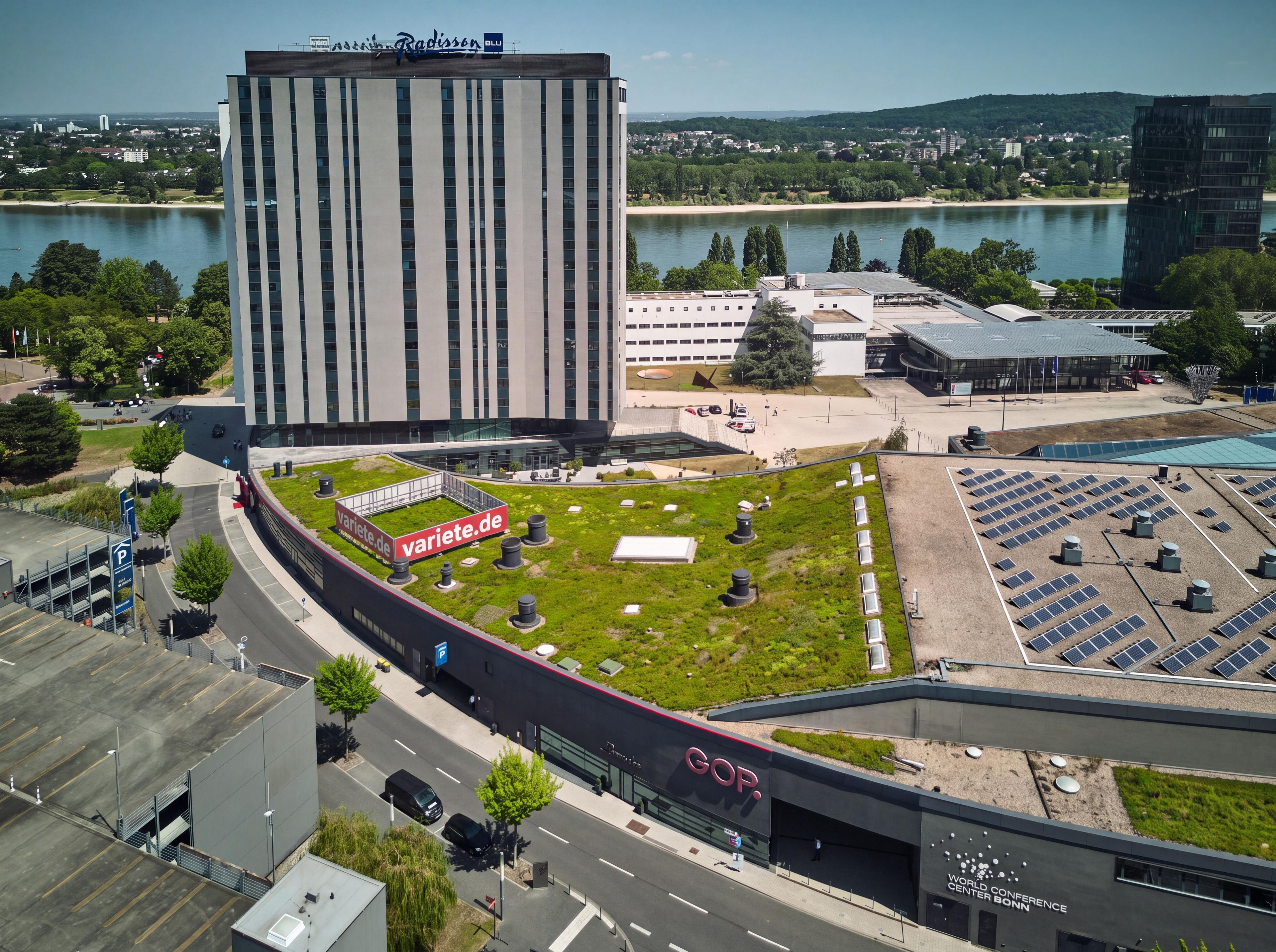 A modern building with a flat roof, a parking area, and a green space with solar panels.