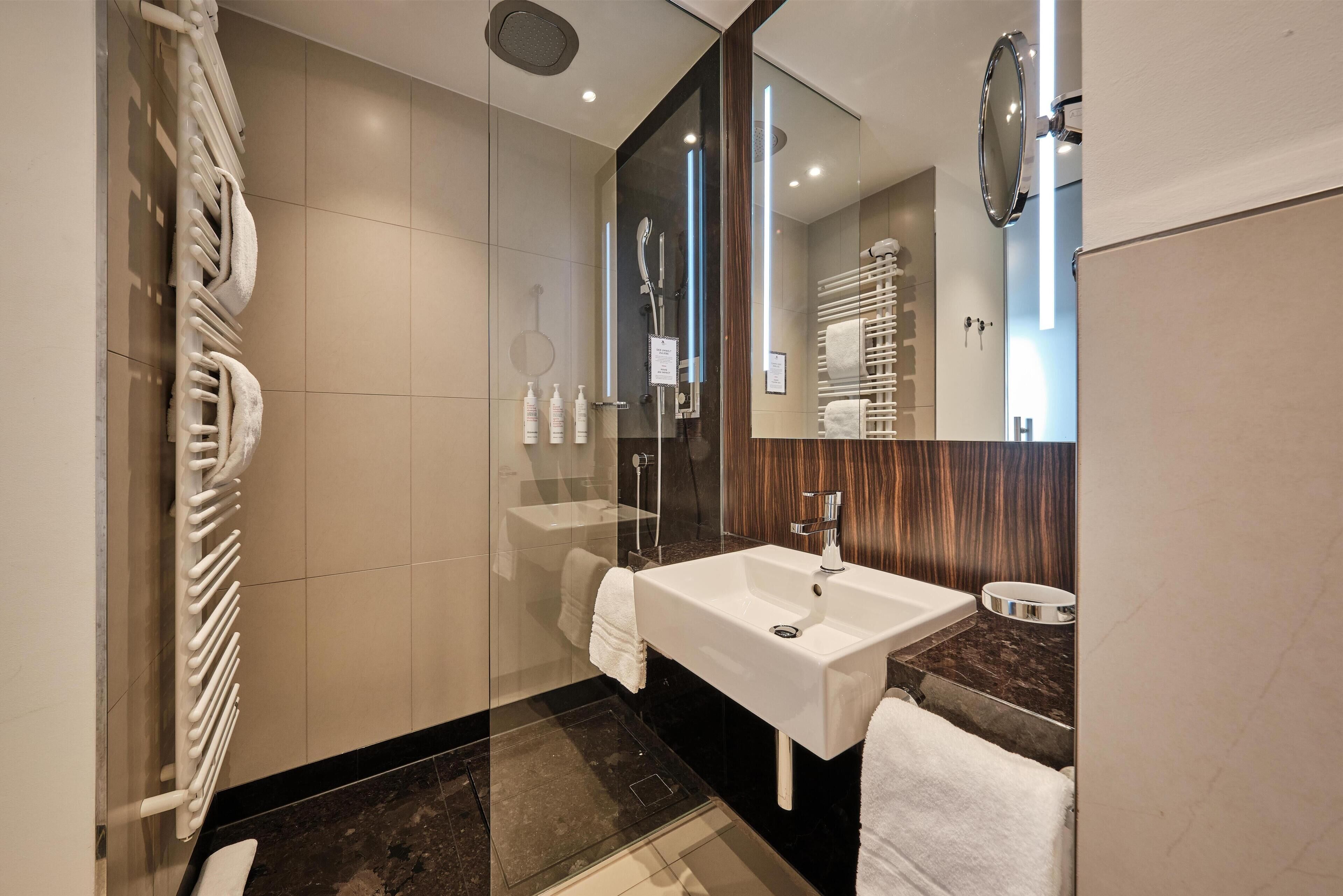 A modern bathroom with a large mirror, a white sink, and a glass shower enclosure.