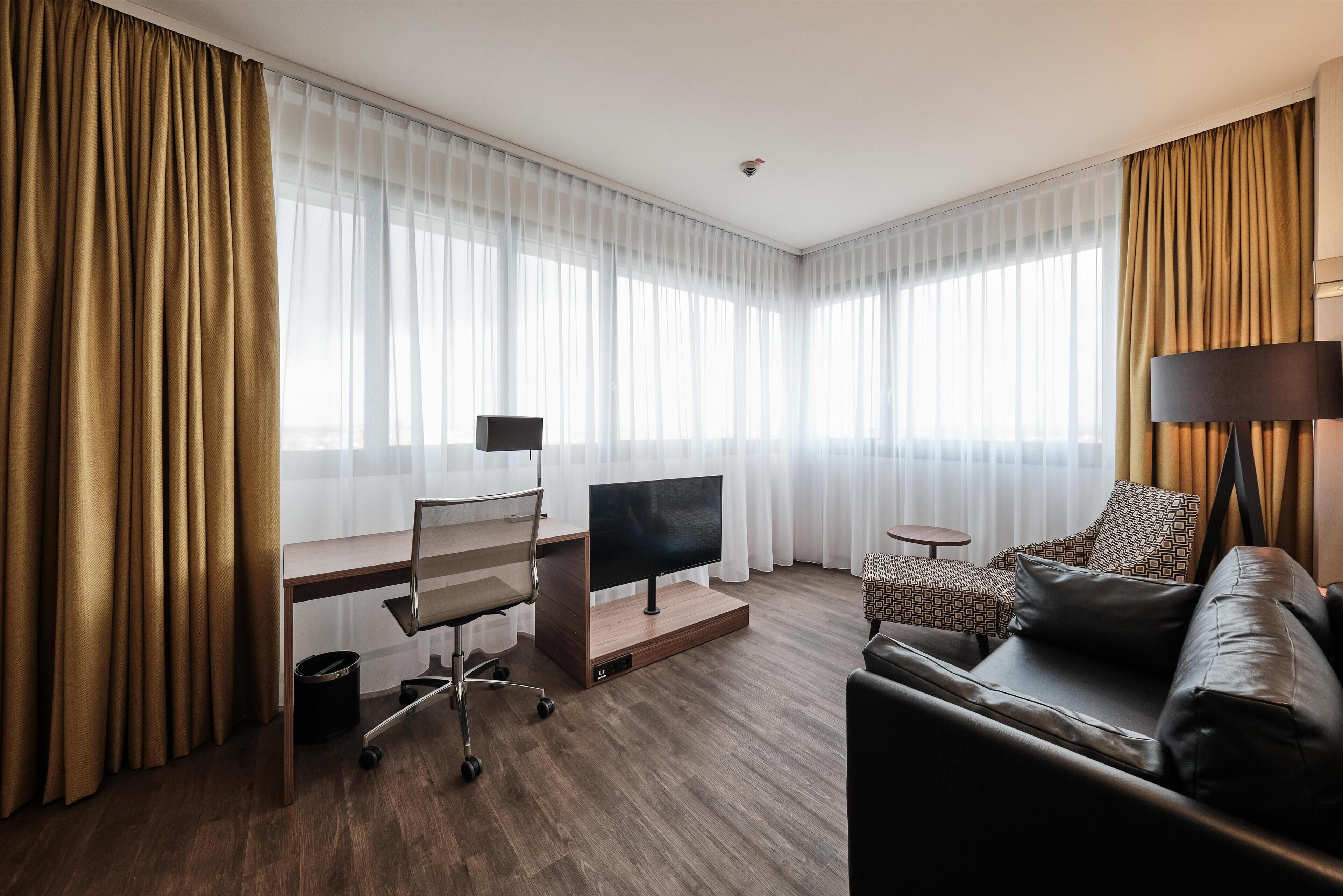 Habitación de hotel con escritorio, televisor de pantalla plana, sofá y lámpara.