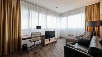 Habitación de hotel con escritorio, televisor de pantalla plana, sofá y lámpara.