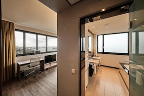 Habitación de hotel moderna con un ventanal grande, un escritorio, un baño con bañera y cabina de ducha de vidrio.