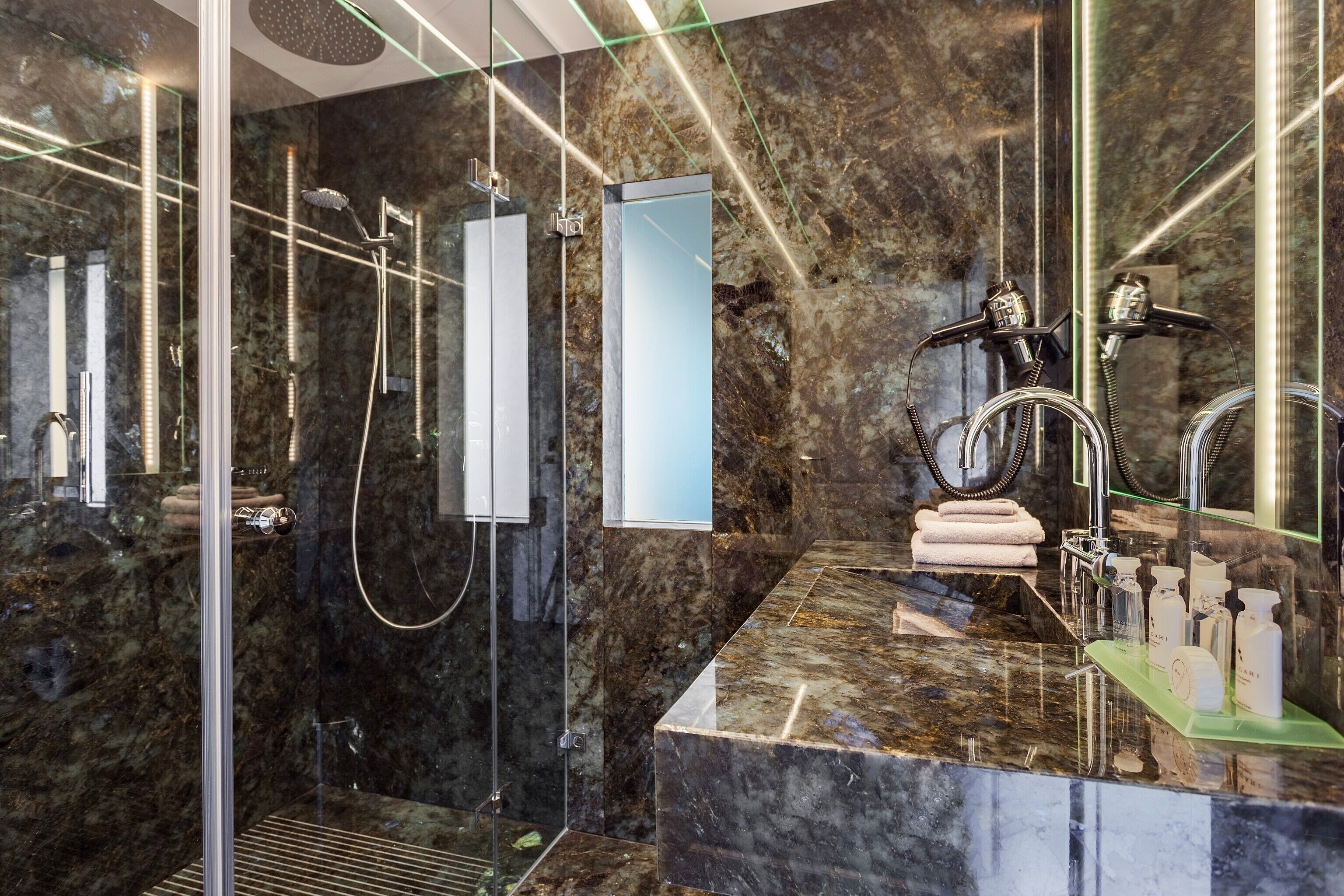 Un bagno moderno con cabina doccia in vetro, un piano di lavoro in marmo e un grande specchio.