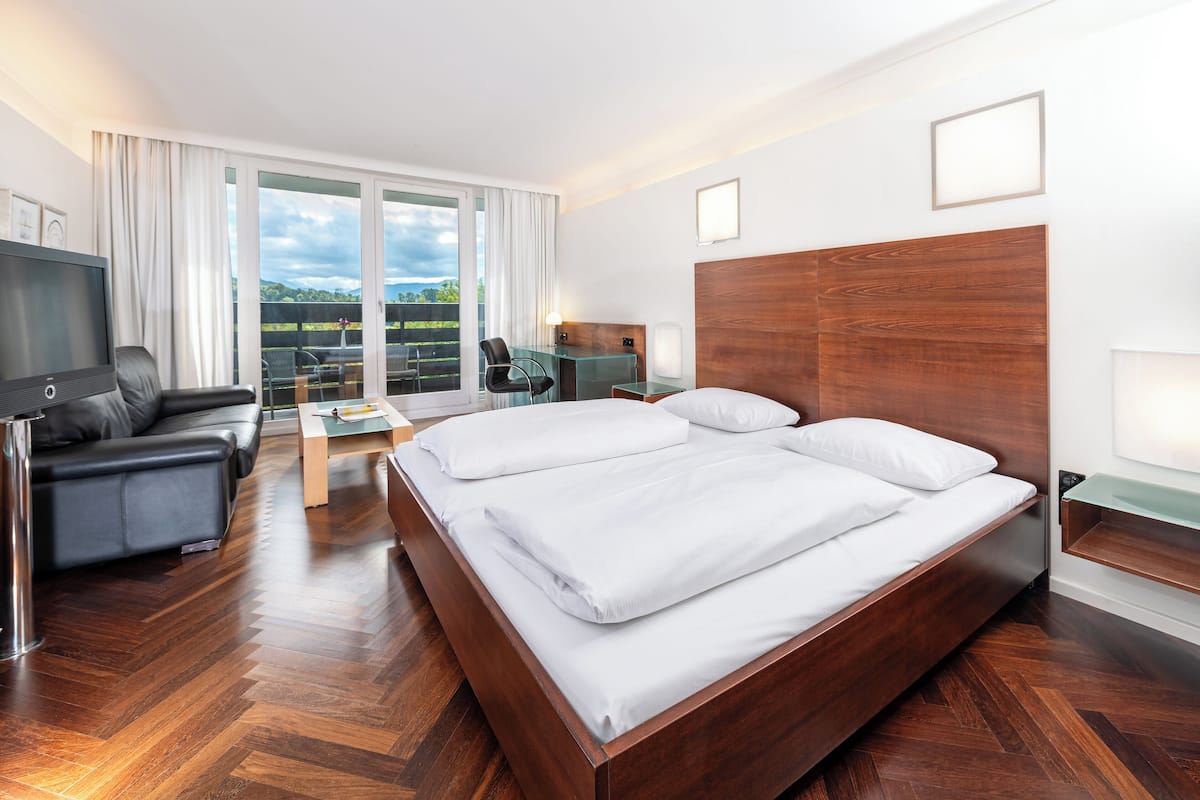 Ein modernes Hotelzimmer mit einem großen Bett, einer Couch, einem Fernseher und einem Balkon mit Blick ins Freie.