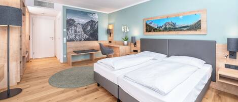 Una habitación de hotel moderna con suelo de madera, una cama doble, un escritorio, una silla y dos cuadros en las paredes.