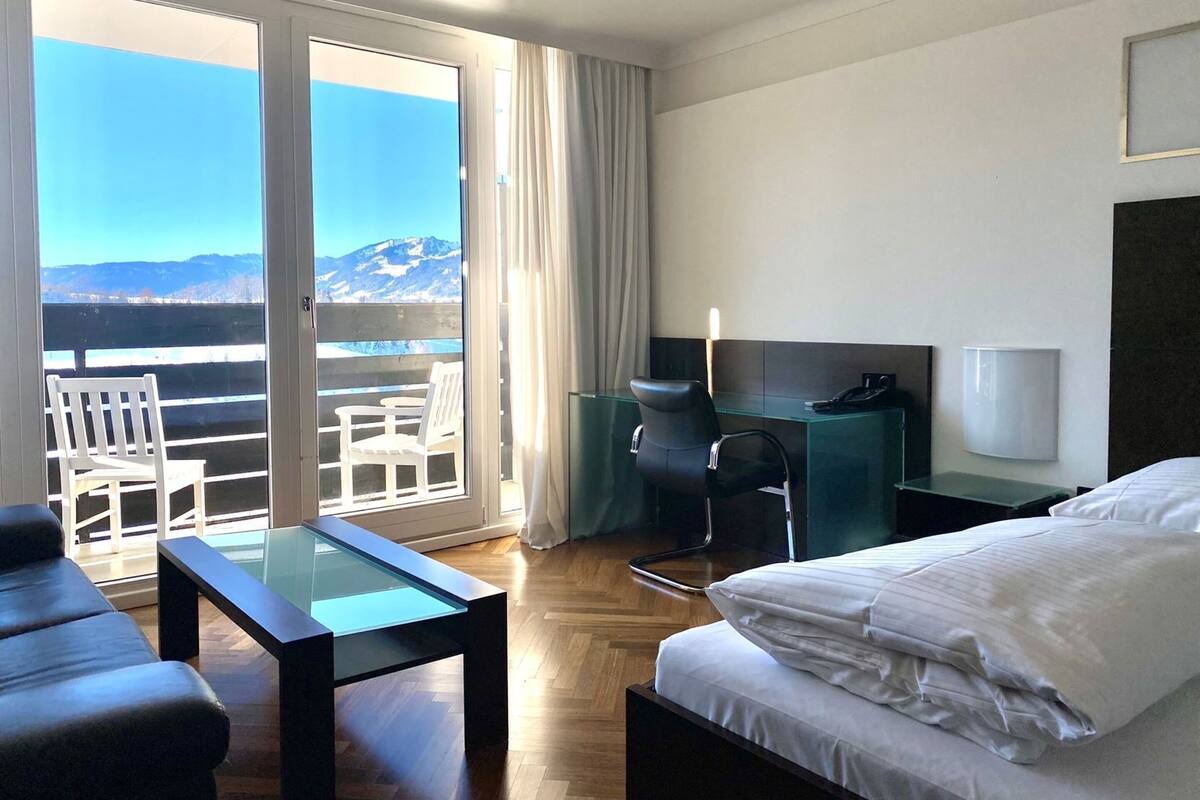 Ein Hotelzimmer mit Bett, Schreibtisch, Stuhl und einem Balkon mit Bergblick.