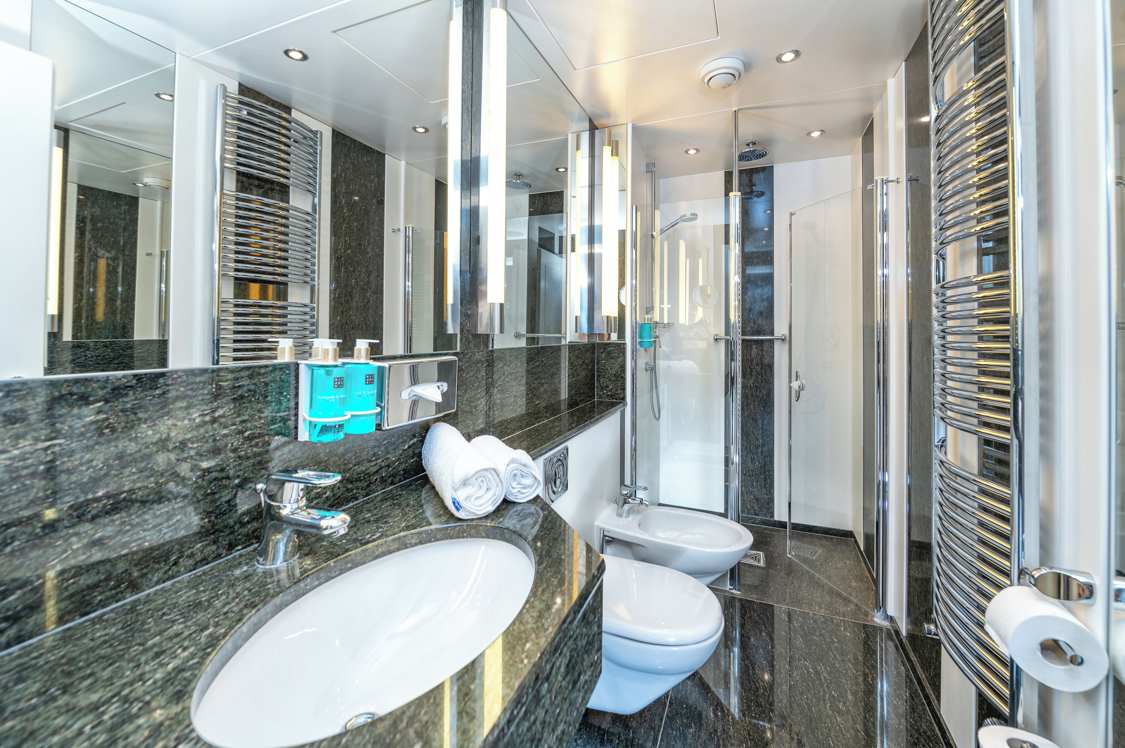 A modern bathroom with a large sink, two toilets, a glass shower enclosure, and a mirror with chrome fixtures.