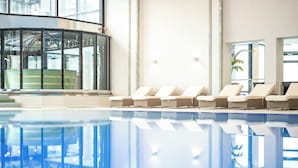 A swimming pool with lounge chairs and a glass-enclosed area with a view of the outside. - Allgäu Stern Hotel (Sonthofen)