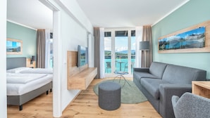 A modern hotel room with a bed, a grey sofa, a round ottoman, and a TV. - Allgäu Stern Hotel (Sonthofen)