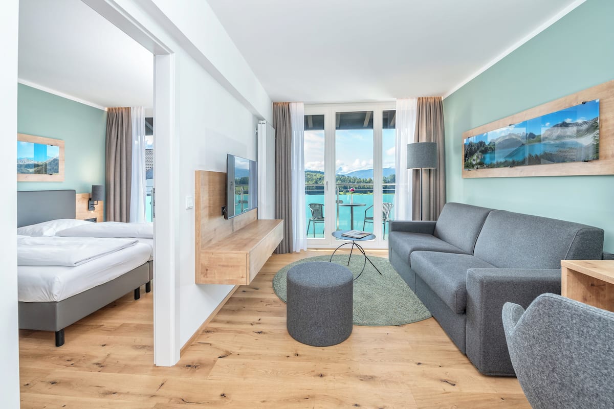 Ein modernes Hotelzimmer mit einem Bett, einem grauen Sofa, einem runden Ottomanen und einem Fernseher.
