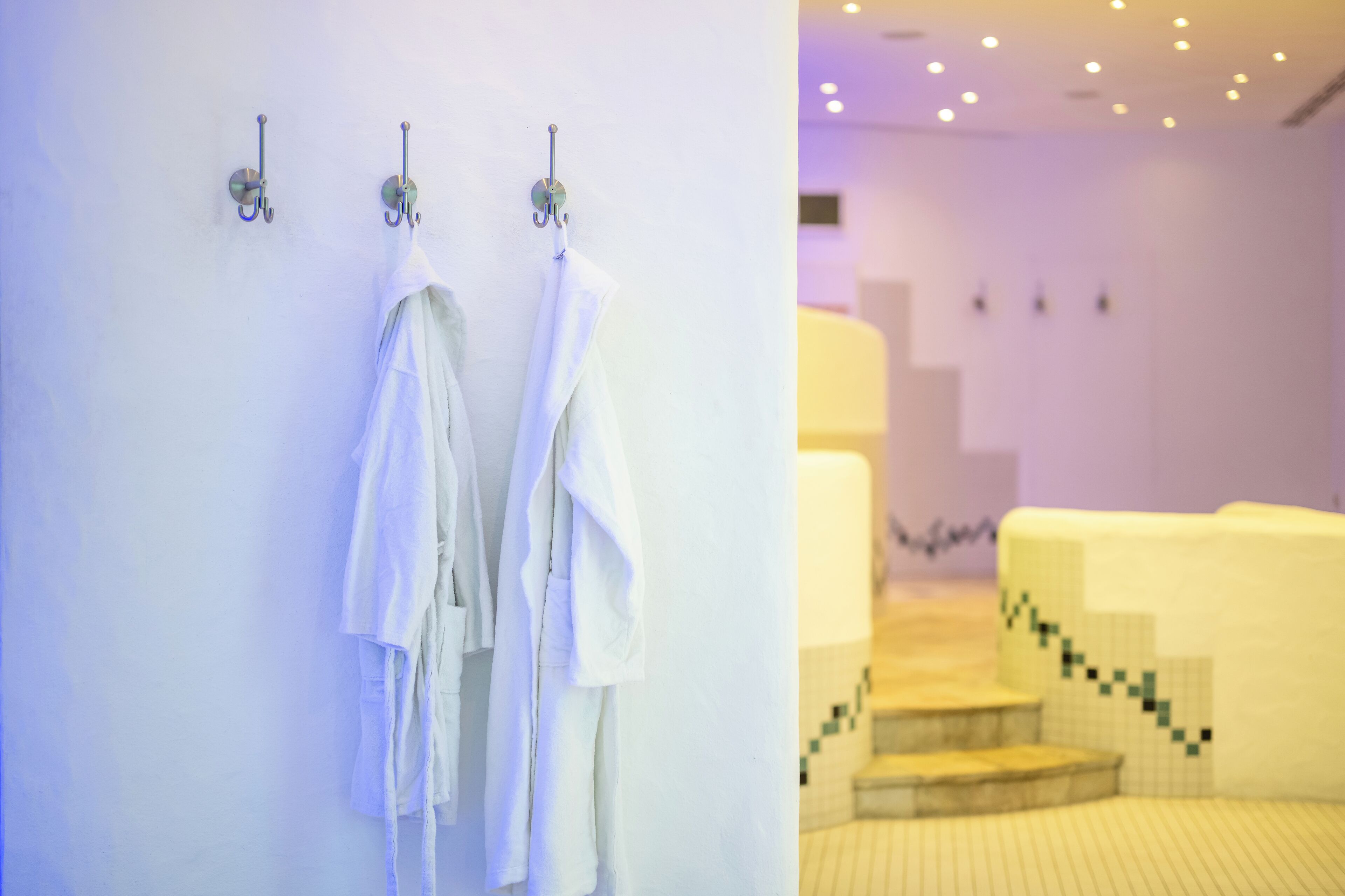 A bathroom with white towels hanging on hooks and a tiled floor with a geometric pattern.