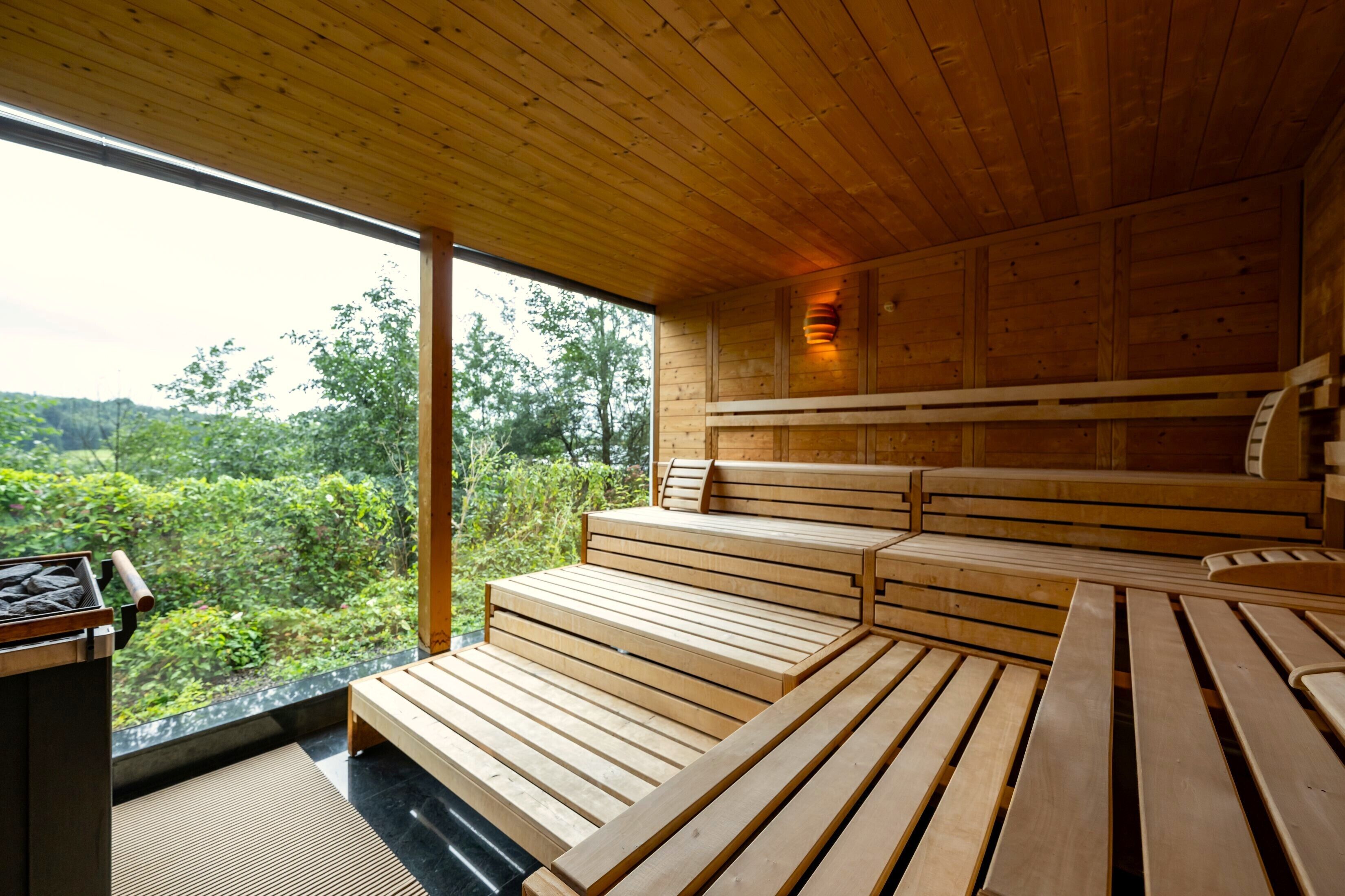 Un interior de madera con una zona de asientos tipo banco, vistas a la vegetación exterior y una pequeña mesa con un recipiente de piedra.