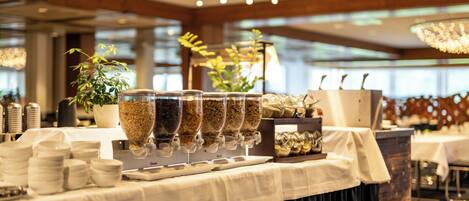 A buffet setup with multiple food dispensers, a potted plant, and a chandelier.