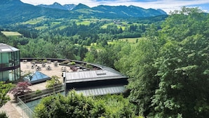 A modern building with a glass conservatory, outdoor seating, and a view of a mountainous landscape. - Allgäu Stern Hotel (Sonthofen)