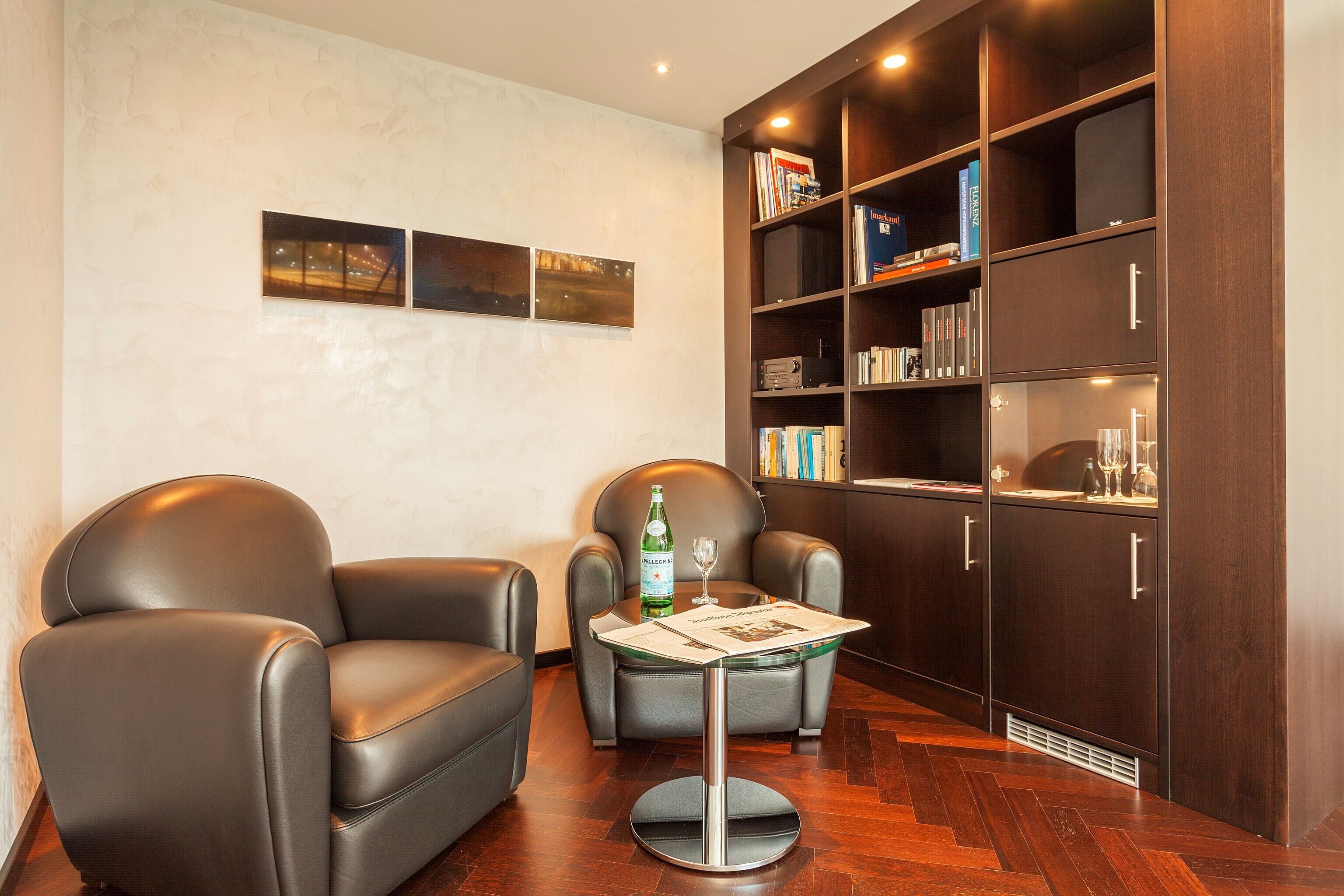 Una habitación moderna con sillones de cuero, una mesa de vidrio, una estantería y obras de arte en la pared.