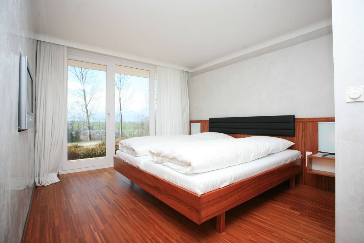 Ein Schlafzimmer mit einem hölzernen Bett, einem Nachttisch und einem großen Fenster mit Vorhängen.