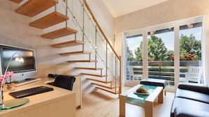 A modern living room with a wooden staircase, a flat-screen TV, a glass coffee table, and a sofa. - Allgäu Stern Hotel (Sonthofen)