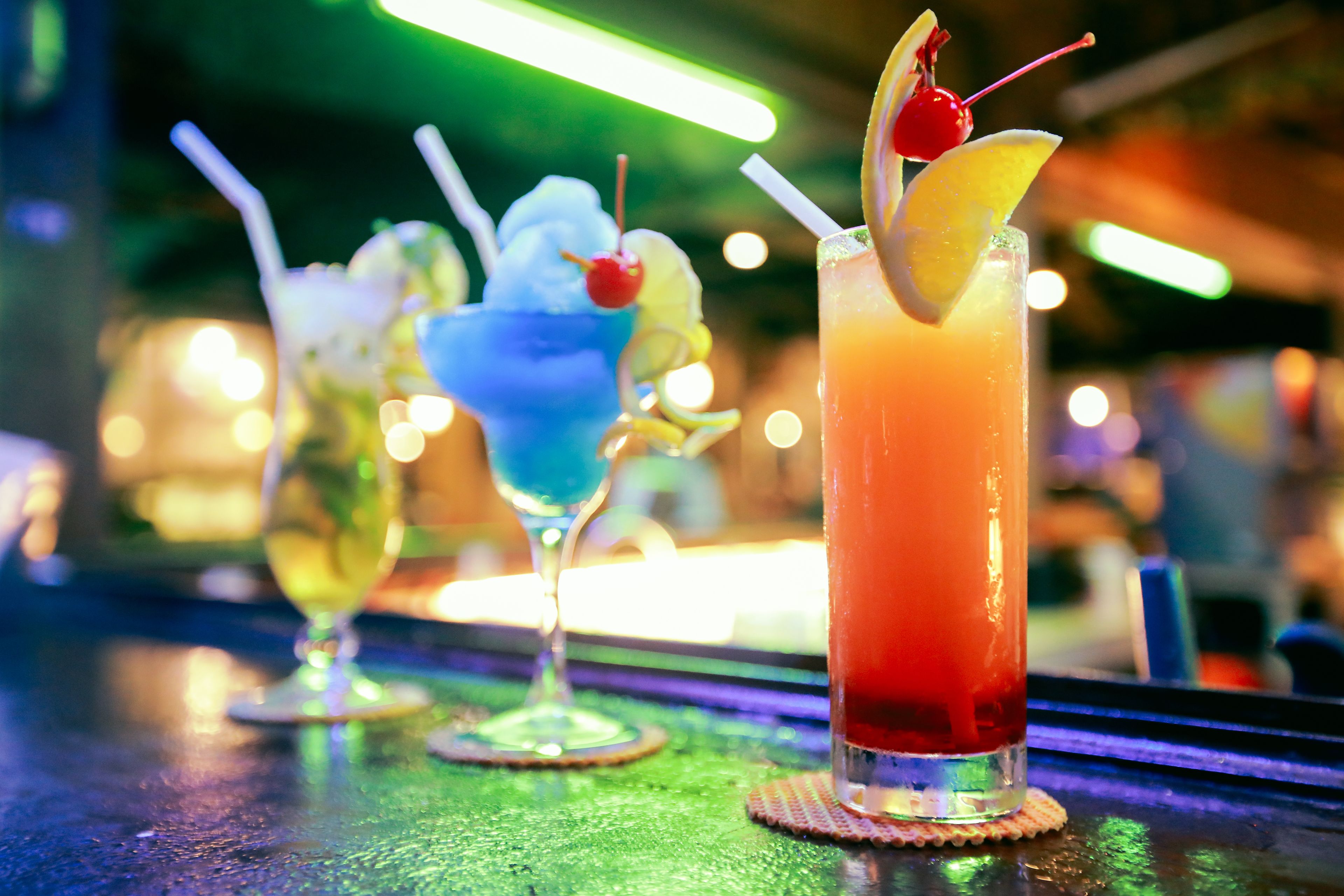 Tres bebidas sobre una barra con fondo desenfocado.