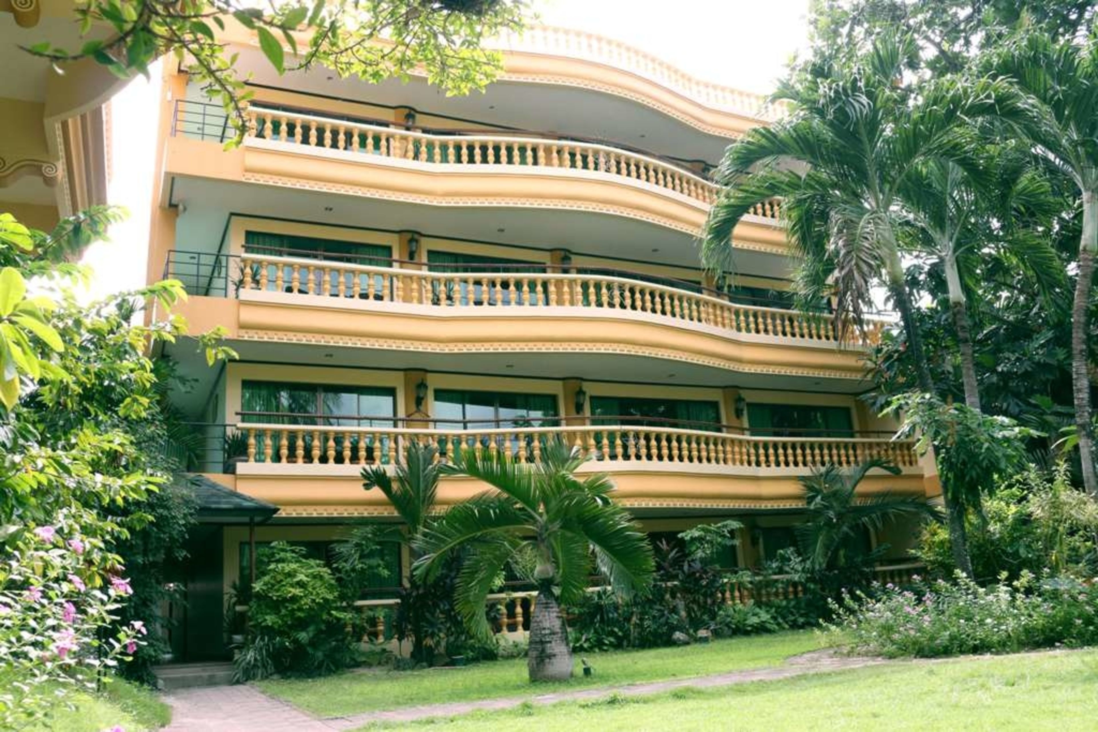 Um hotel com vários andares e varandas, rodeado por vegetação exuberante e palmeiras.