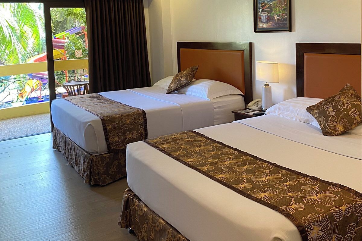 A hotel room with two beds, a painting, and a view of a playground.
