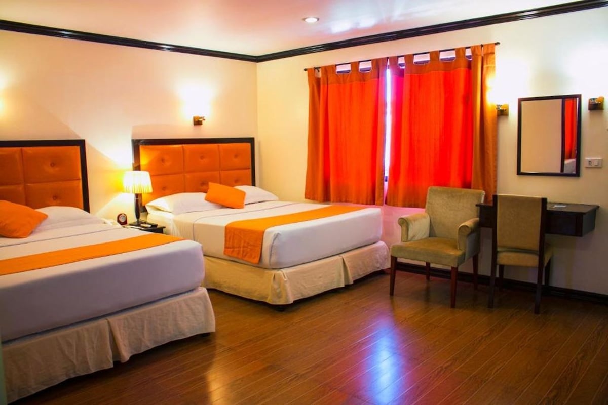 A hotel room with two beds, a chair, a desk, and a mirror.