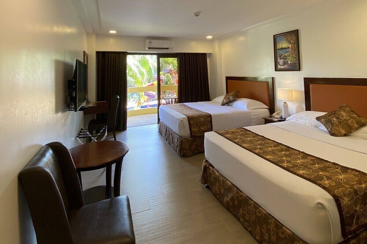 A hotel room with two beds, a desk, a chair, and a TV.
