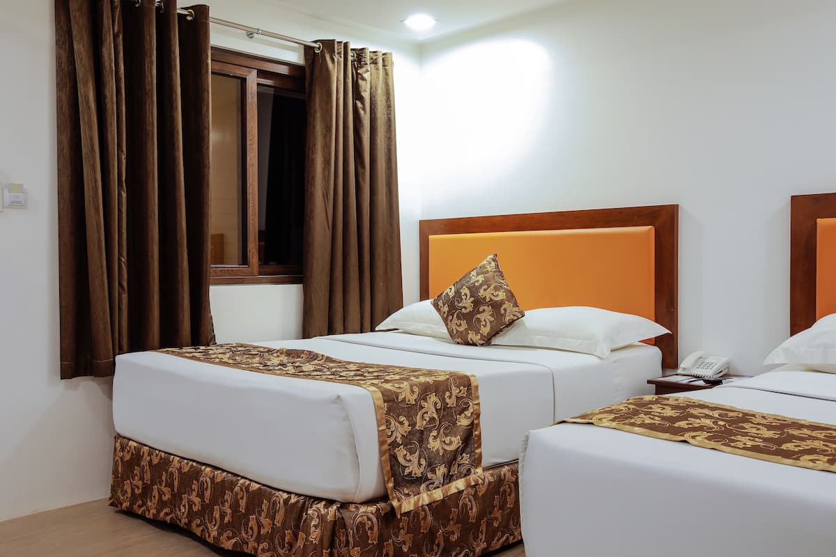 A hotel room with two beds, brown curtains, a wooden headboard, and a telephone on the nightstand.