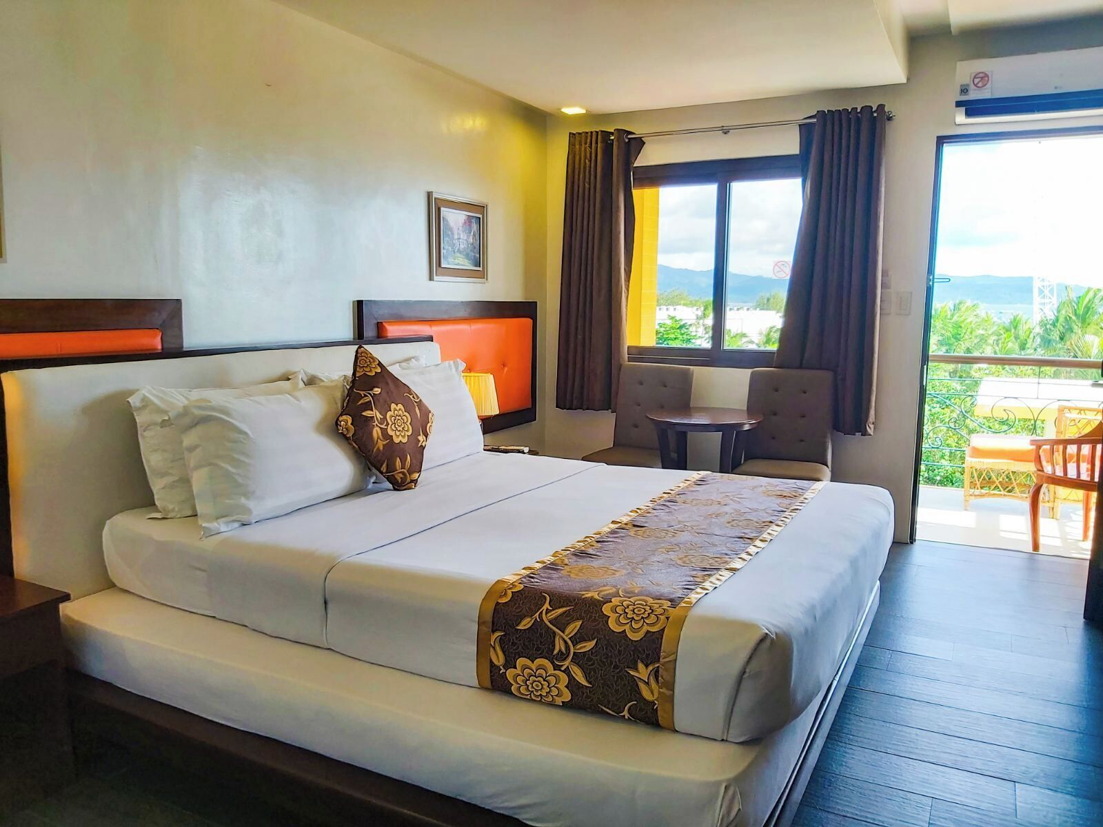 A hotel room with a bed, a small table, a chair, and a view of the outdoors.