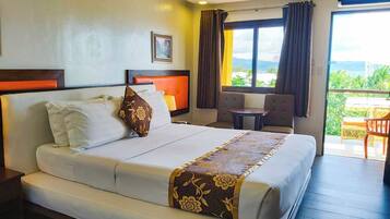 A hotel room with a bed, a small table, a chair, and a view of the outdoors.