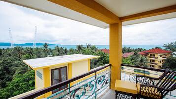 Un balcón con un edificio amarillo, vista al mar y una silla.