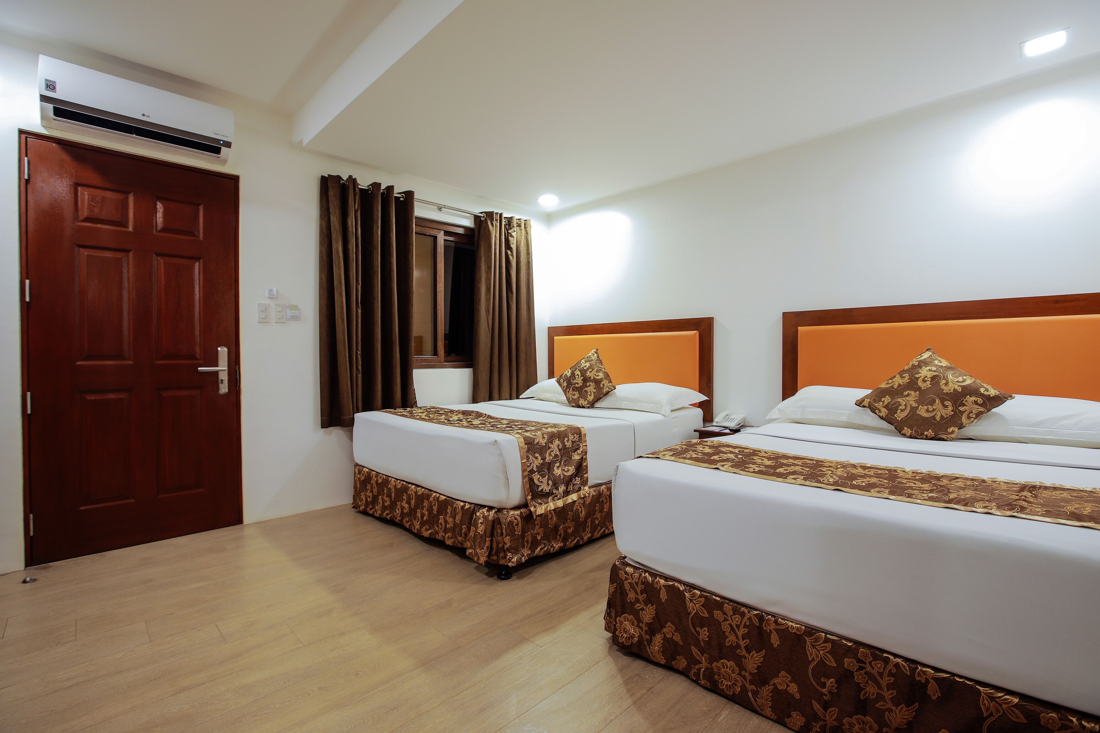 A hotel room with two beds, a wooden door, and an air conditioning unit.