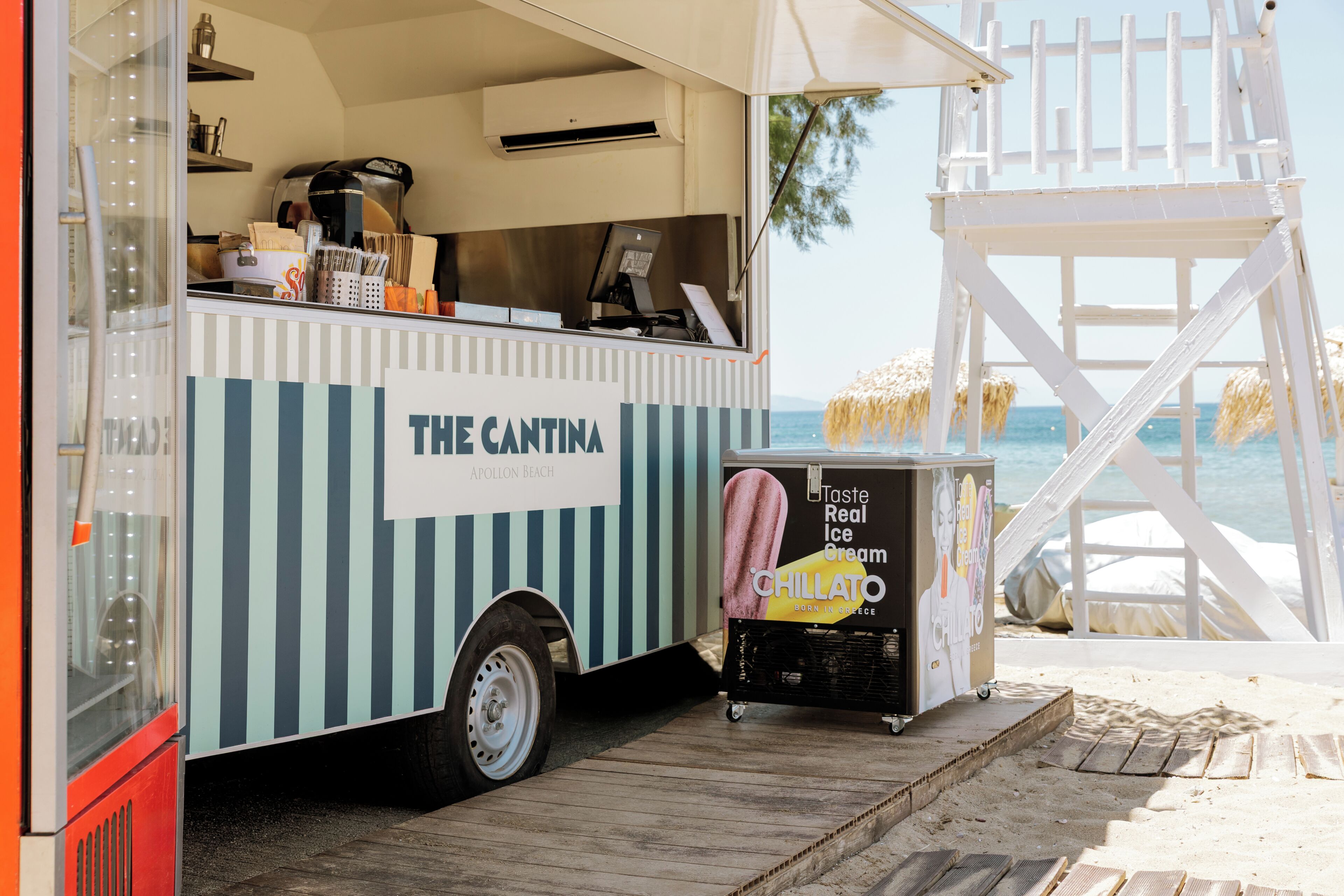 A food truck named 'The Cantina' with a menu display, parked on a wooden deck with a beach view.