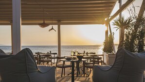 A terrace with outdoor seating, tables, and a view of the sea at sunset. - Divani Escape- Adults only (Vari-Voula-Vouliagmeni)