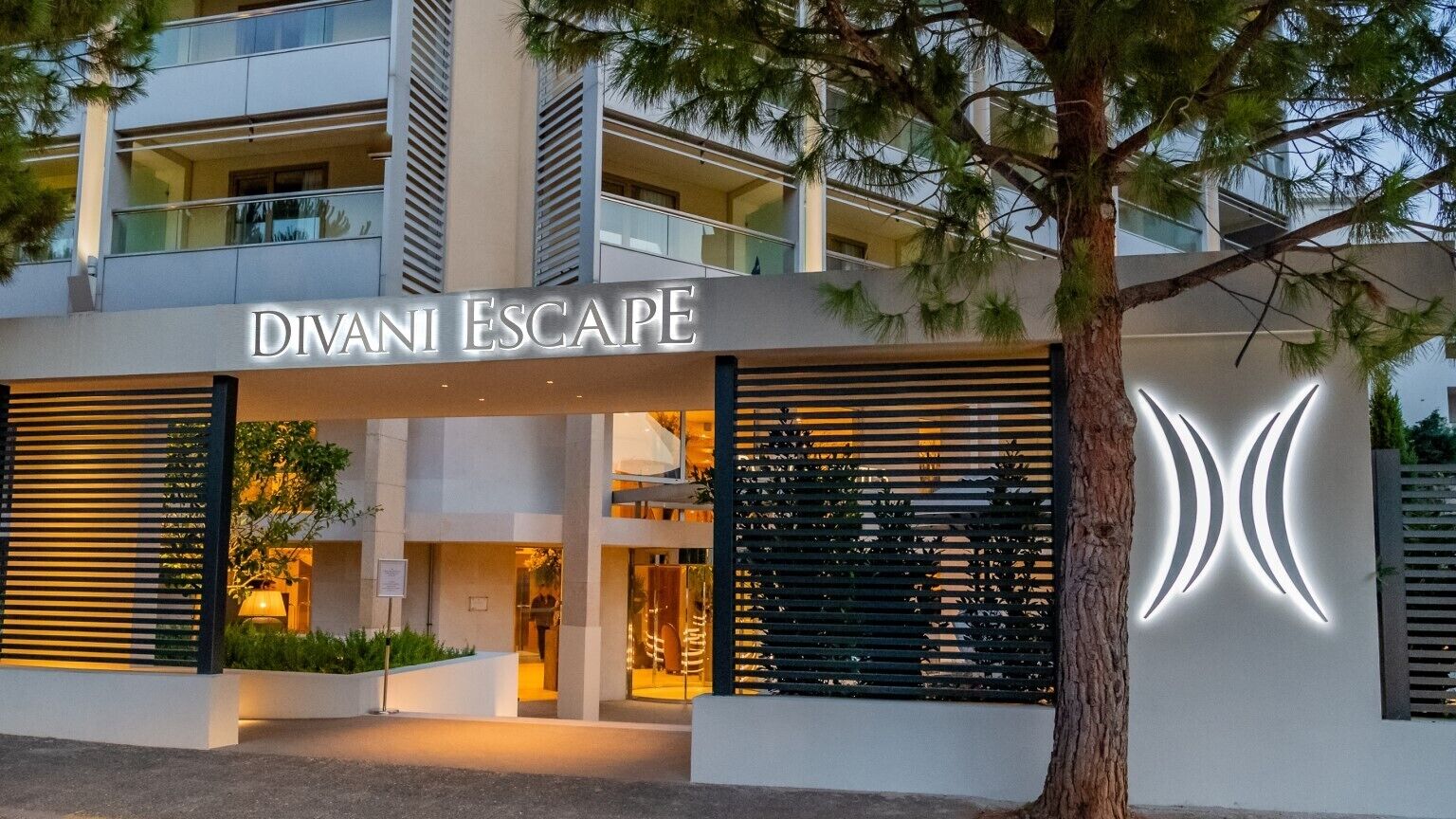 Ein modernes Gebäude mit der Aufschrift 'DIVANI ESCAPE', das ein Hotel oder Resort kennzeichnet.