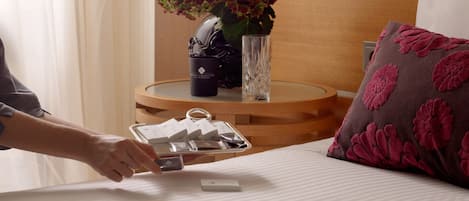A neatly made bed with a pillow, a bedside table with a vase of flowers, and a tray with items on it.