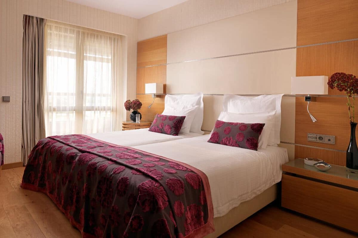 A hotel room with a large bed, two bedside tables, a chair, a nightstand, and a window with curtains.