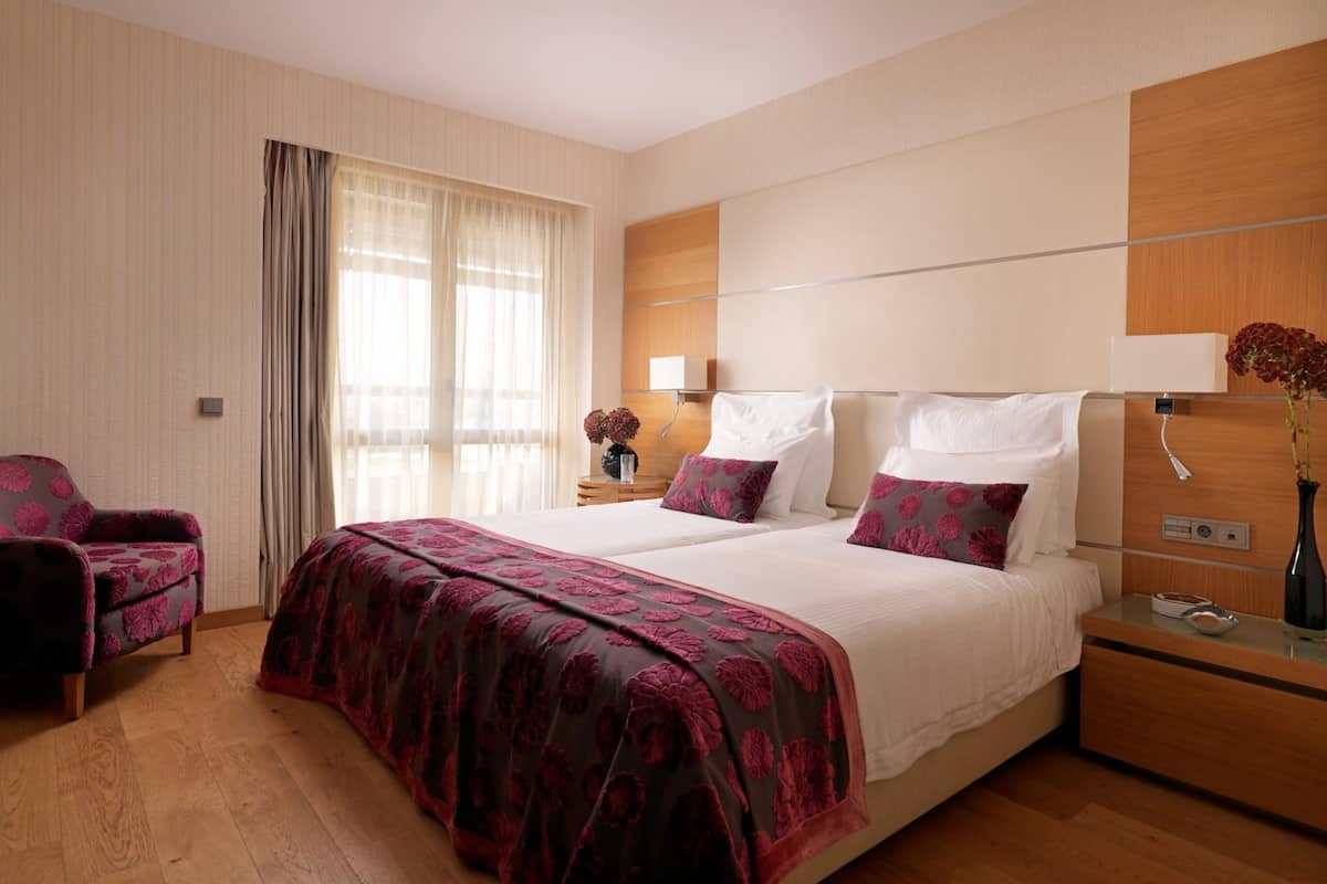A hotel room with a large bed, a bedside table, a chair, and a window with curtains.